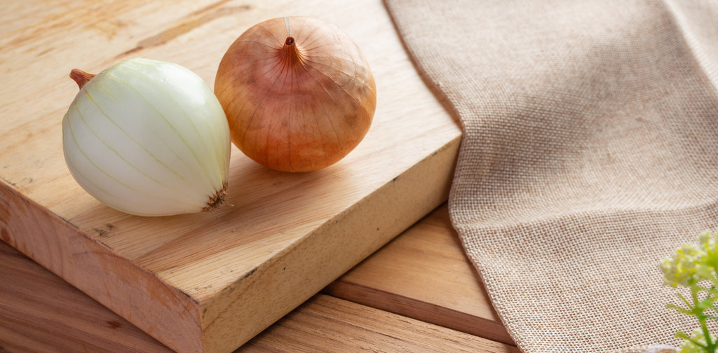 Two onions on a light brown wood cutting board.