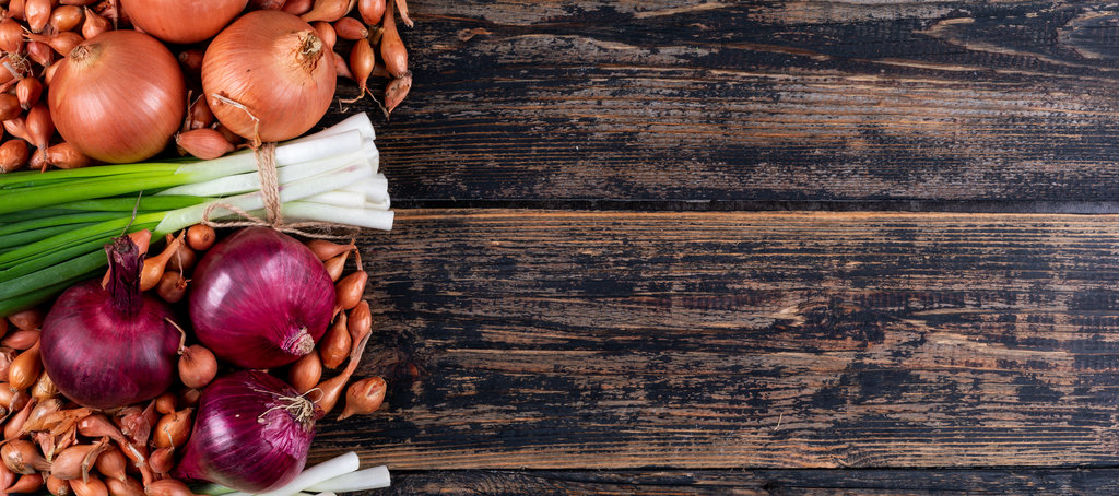 Set of red onions, shallots, spring onions or scallions and onions on a dark wooden background. top view. space for text.