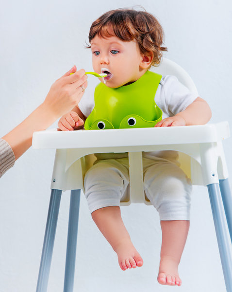 Happy baby boy sitting and eating Toddler eating puree with a spoon