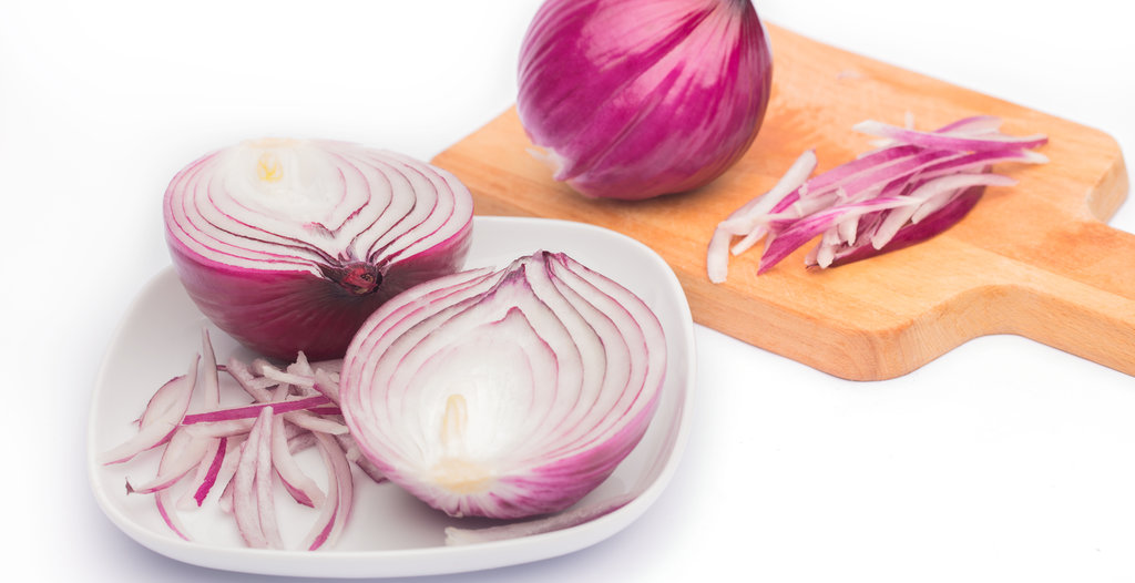 close up of sliced red onion and whole red onion on a wooden table.