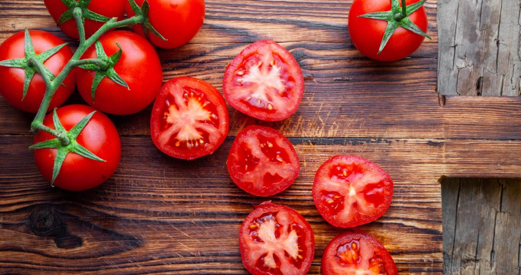 Some tomatoes and slices with knife on a wooden cutting board top view. tomato face mask