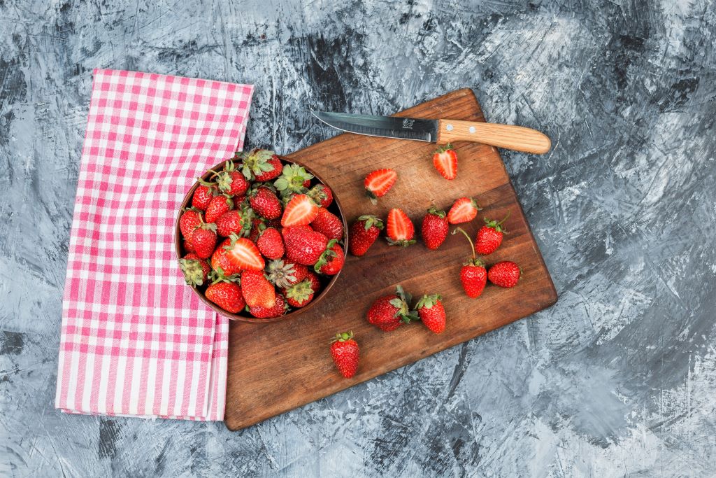 flat-lay-bowl-strawberries-knife-wooden-cutting-board-with-red-gingham-tablecloth-dark-blue-marble-surface-horizontal
