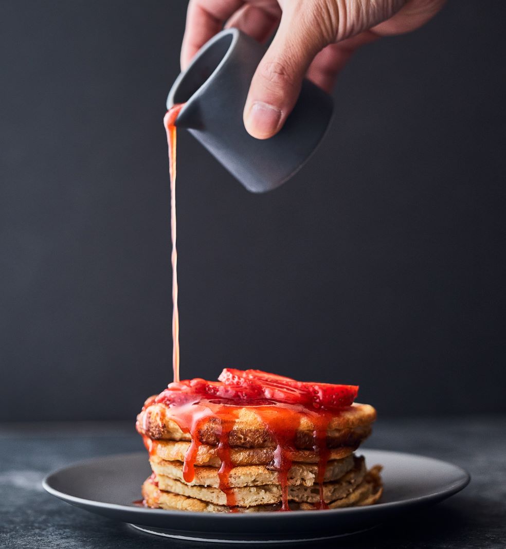 man pouring strawberry puree on pancakes