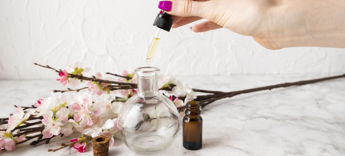 high-angle-hand-using-body-seum geranium flowers and oil in dropper