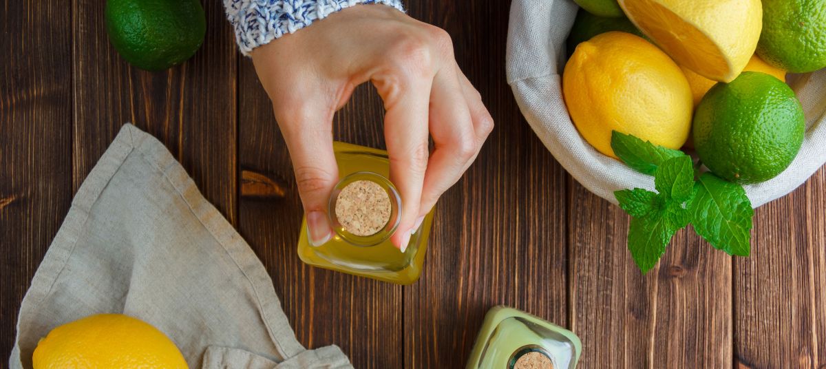 set-white-cloth-hands-holding-lemon-juice-bottle-lemons-basket-wooden-surface-top-view lemon essential oil